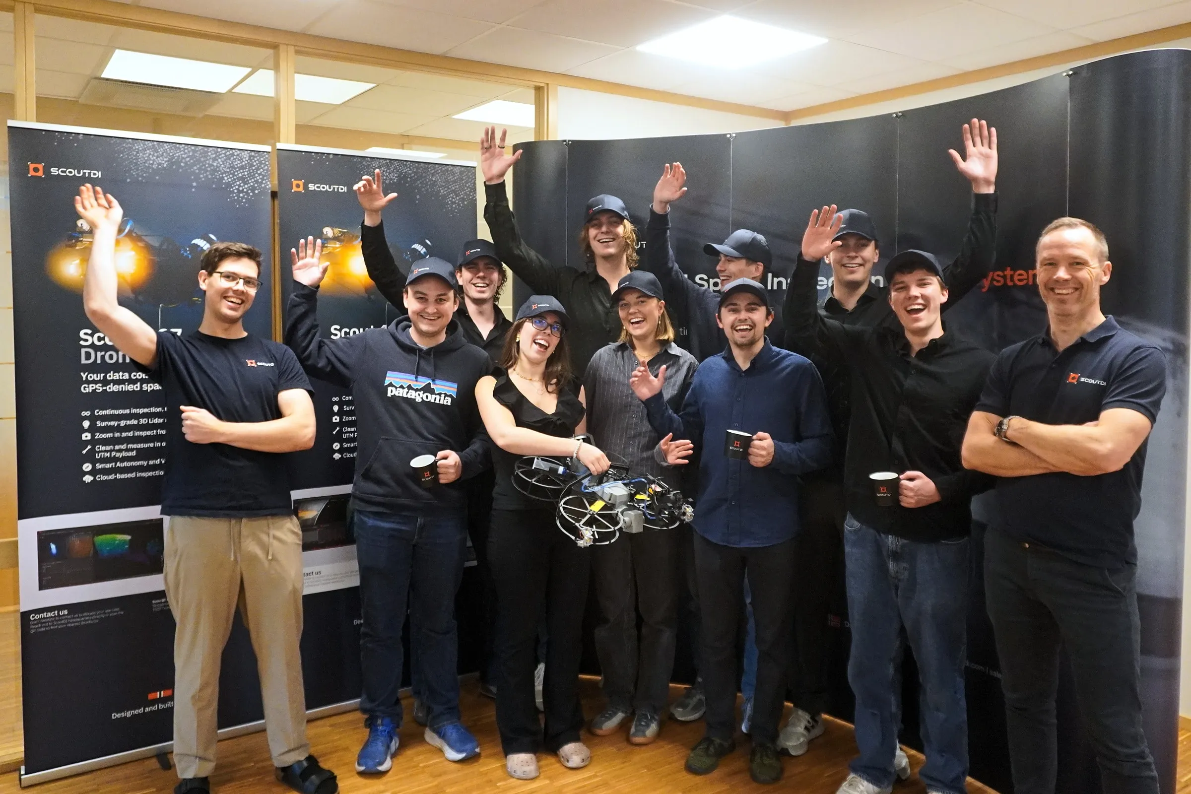 The Mobula team waving in front of ScoutDI banners at ScoutDI's office in Trondheim, one of them holding a ScoutDI drone